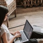Mentorship Program - Young barefoot woman using laptop on floor near books in stylish living room